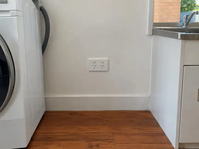 Double power point on a white wall above timber flooring beside a laundry appliance in Bundall