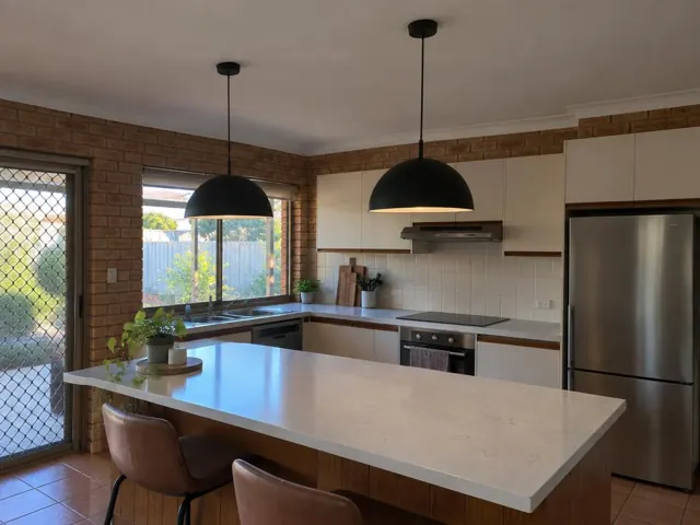 Two black pendant lights over a kitchen island in a brick-walled home kitchen in Carrara