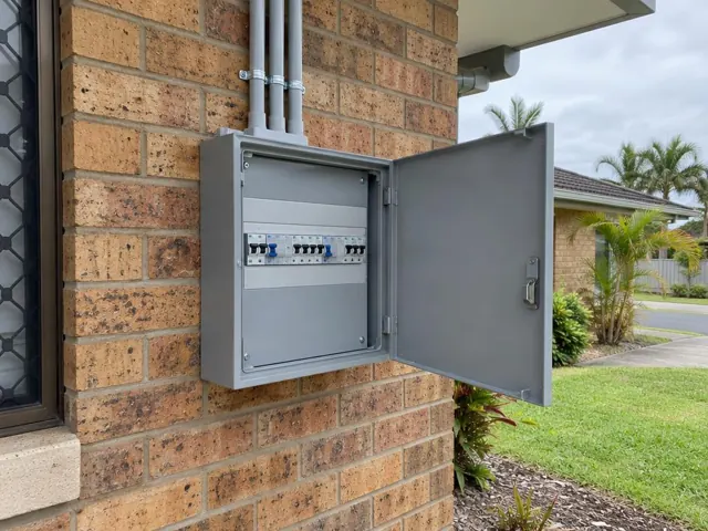 Exterior electrical switchboard on a brick house wall with the door open in Mermaid Waters